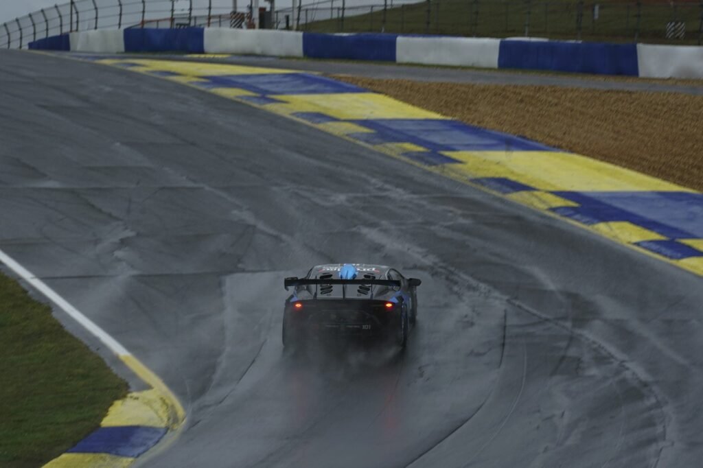 A race car driving through a corner on a wet, rain-soaked track.